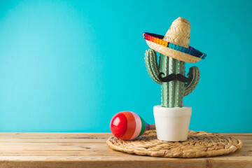 Mexican party concept with cactus, maracas and sombrero hat on wooden table over blue background....