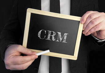 A businessman holds up a chalkboard with text CRM