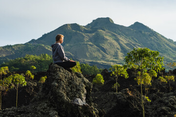 A young girl, sitting in a lotus position, arms to the sides, meditates in the mountains, in the first rays of the sun in the morning.