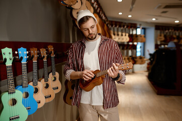 Man musician buying ukulele guitar at musical instrument shop