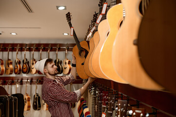 Young male owner of musical instrument shop putting guitar at display case