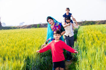 Happy young indian farmer family walking in wheat agriculture field, Parents with children outdoor, Rural india concept.