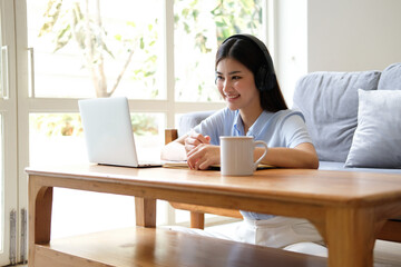 Portrait of Young asian woman wearing headphones using laptop in cafe, writing notes, learning language, watching online business or education concept