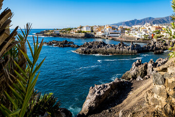 The bay of fishing village Alcalá bathed in warm afternoon sunlight is showcased in a panoramic...
