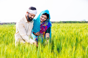 Happy young indian farmer couple touching wheat crop standing at agriculture field in bright sunny day. Copy space. Rural india concept.