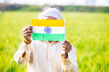 Rural farmer man holding indian and flag while standing at agriculture field, Independence day or Republic day.