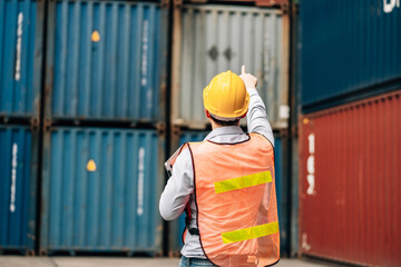 Asian technician dock worker in protective safety jumpsuit uniform and with hardhat and use laptop computer at cargo container shipping warehouse. transportation import,export logistic industrial