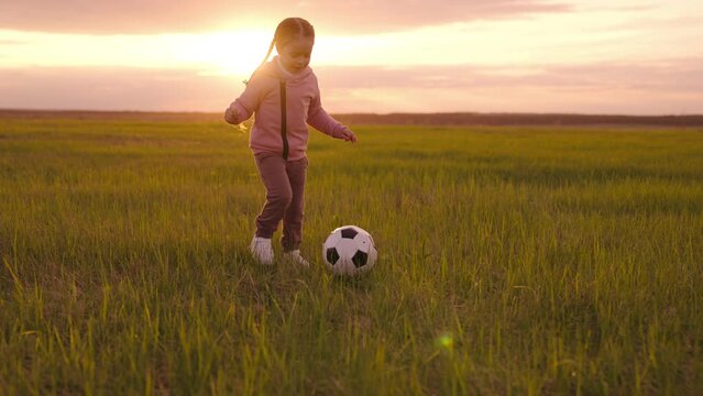 little girl runs across green field kicking ball sunset sky. chidhood dream. happy family. cheerful child plays football rays sunlight. football. Kid loves play ball. concept kids football game ball.