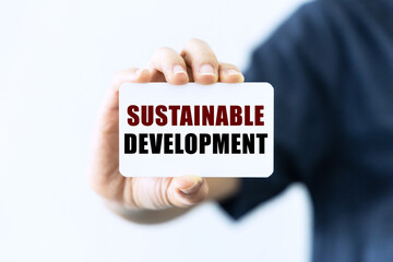 Sustainable development text on blank business card being held by a woman's hand with blurred background. Business concept about sustainable development.