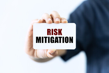 Risk mitigation text on blank business card being held by a woman's hand with blurred background. Business concept about risk mitigation.