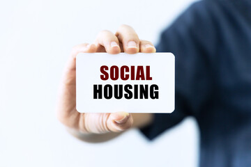 Social housing text on blank business card being held by a woman's hand with blurred background. Business concept about social housing.