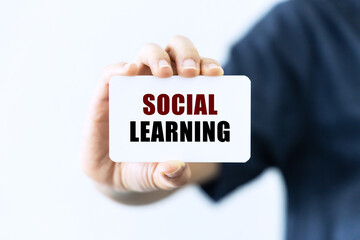 Social learning text on blank business card being held by a woman's hand with blurred background. Business concept about social learning.