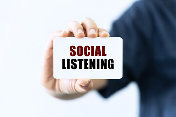 Social listening text on blank business card being held by a woman's hand with blurred background. Business concept about social listening.