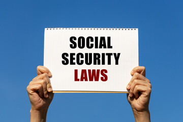 Social security laws text on notebook paper held by 2 hands with isolated blue sky background. This message can be used as business concept about social security laws.