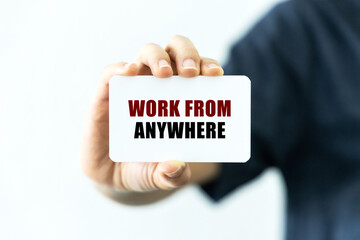 Work from anywhere text on blank business card being held by a woman's hand with blurred background. Business concept about working remotely.