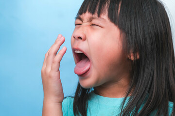 Little asian girl covering her mouth to smell the bad breath. Child girl checking breath with her hands. Oral health problems or dental care concept.