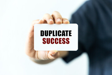 Duplicate success text on blank business card being held by a woman's hand with blurred background. Business concept about duplicate success.