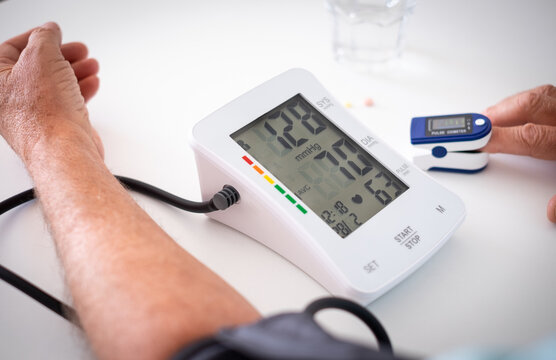 Old senior man using medical device to measure blood pressure - elderly man suffering from hypertension sitting at home table taking care of his health