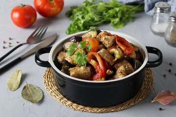 Braised pork with eggplant and tomatoes in ceramic dish on gray background