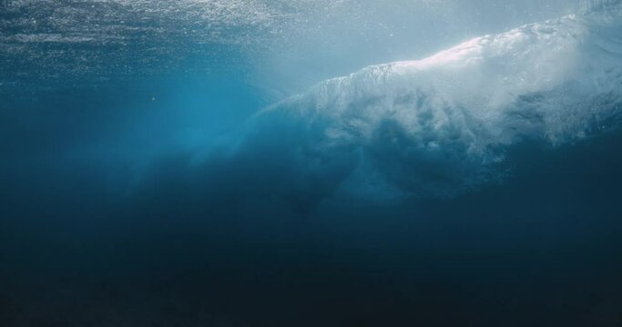 Wave breaking in ocean and sunlight. Underwater view of powerful barrel wave with foam