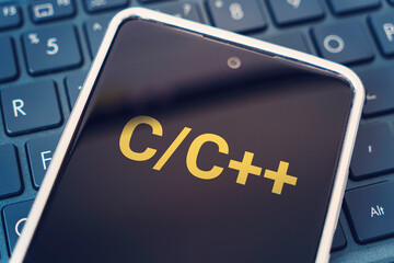 C Programming language for mobile development, concept. Smartphone on the laptop keyboard, the...