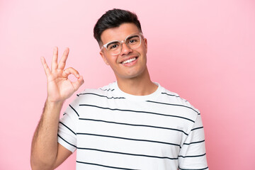 Young caucasian handsome man isolated on pink background With glasses and doing OK sign