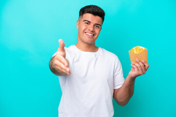 Young caucasian man catching french fries isolated on blue background shaking hands for closing a good deal