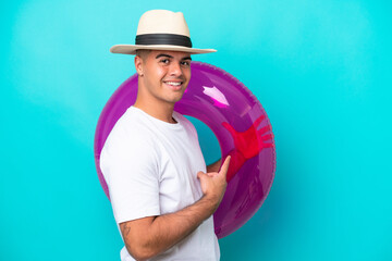 Young caucasian man holding air mattress isolated on blue background and pointing it