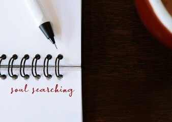 Notebook on copy space wood with text written SOUL SEARCHING, means taking step back to examine...