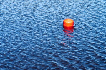 Red anchor buoy in cylinder shape lies on a ripple sea surface. Water safety theme.
