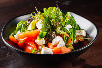 Fresh greek salad with tomato, cucumber, bel pepper, olives and feta cheese in black bowl