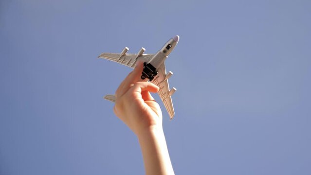 Close-up of a small child holding a toy model airplane in his hand against a blue sky background. A child plays with an airplane in the summer on vacation. The concept of travel.
