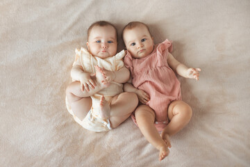 Top view of two cute baby twin girls 6 month old lying together on comfortable and soft bed with...