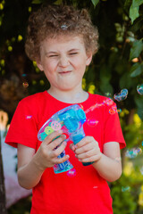 A curly-haired boy in a red T-shirt plays with a gun that generates soap bubbles. Children's game...