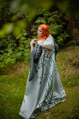 A young woman in a cloak, with a staff and a green dress in the form of a druid. Forest witch with...