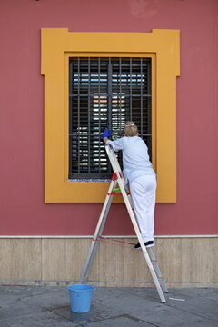 Una señora de la limpieza trabaja en una escalera limpiando una ventana.