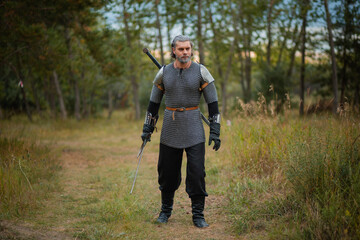 an old warrior in chain mail with a sword is looking for prey in the forest.