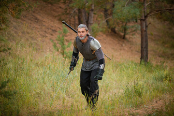 an old warrior in chain mail with a sword is looking for prey in the forest.