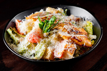 Caesar salad with croutons, cheese, eggs, tomatoes and grilled chicken on black wooden table