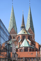 Obraz premium Lubeck Marienkirche or St. Mary Church, historic medieval basilica built in north German Brick Gothic with two monumental towers, seen from the west with reflections in a modern glass facade