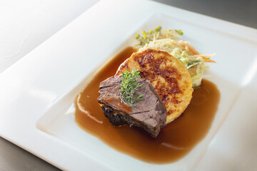 Roast deer, flat bread dumpling and round shaped cabbage vegetable with brown sauce and thyme garnish on a white plate, main course in a menu, copy space, selected focus