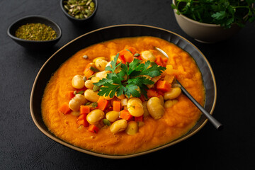 Healthy lunches, tomato and carrot puree soup, beans with pumpkin seeds, healthy tasty legumes, view of a plate of soup on a black background