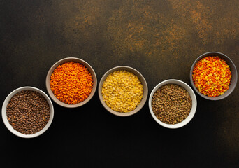 Multicolored lentils in bowls on a brown background, yellow and brown, green and orange lentils, healthy legumes, top view, copy space