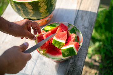 Cutting watermelon man's hand  on a wooden table. Men's hands in the process of slicing watermelon in summer on a sunny day.