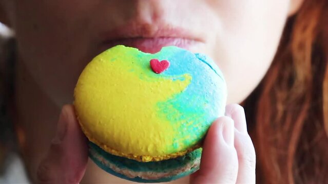 Young girl eating macaroon cake bleu and yellow color with small red heart on it