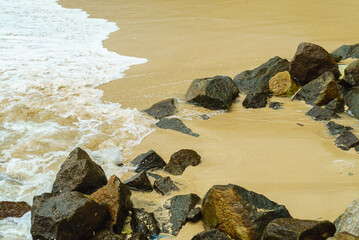 Sandy beach with rough stones and sea waves