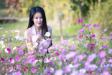 Beautiful woman happy traveler walking in the flowers garden. Young woman smile and relaxing with happy  around outdoor garden. Woman's hand touching and enjoying beauty cosmos flowers.Travel concept.