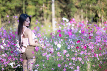 Beautiful woman happy traveler walking in the flowers garden. Young woman smile and relaxing with happy  around outdoor garden. Woman's hand touching and enjoying beauty cosmos flowers.Travel concept.