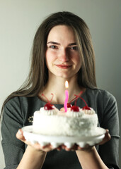 A beautiful girl with a cake in her hands. It's her birthday. White cake, studio shot. Making a birthday wish. A modest holiday