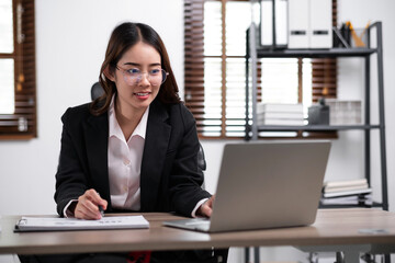 Young confident businesswoman sitting at the office table working on laptop computerr